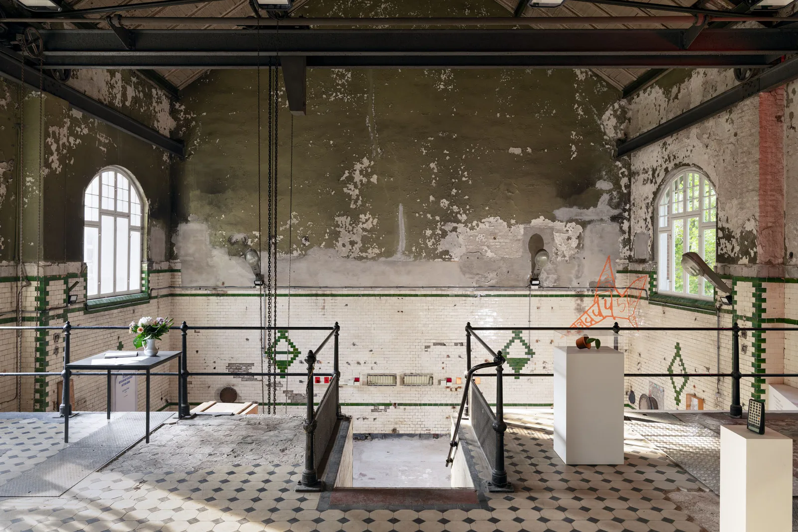 Neue Erinnerungen: Ausstellung in einer alten Halle mit abgeblätterten Wänden, Rundbogenfenstern und Metallgestellen
