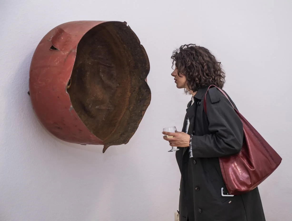 Cheats and Gods, Vernissage: eine Besucherin betrachtet ein rostiges rotes Metallobjekt an der Wand