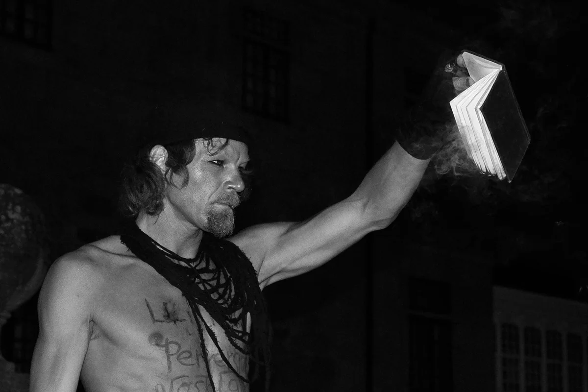 GABRIEL: ein Mann mit Halsketten hält bei Nacht ein aufgeschlagenes Buch in die Höhe