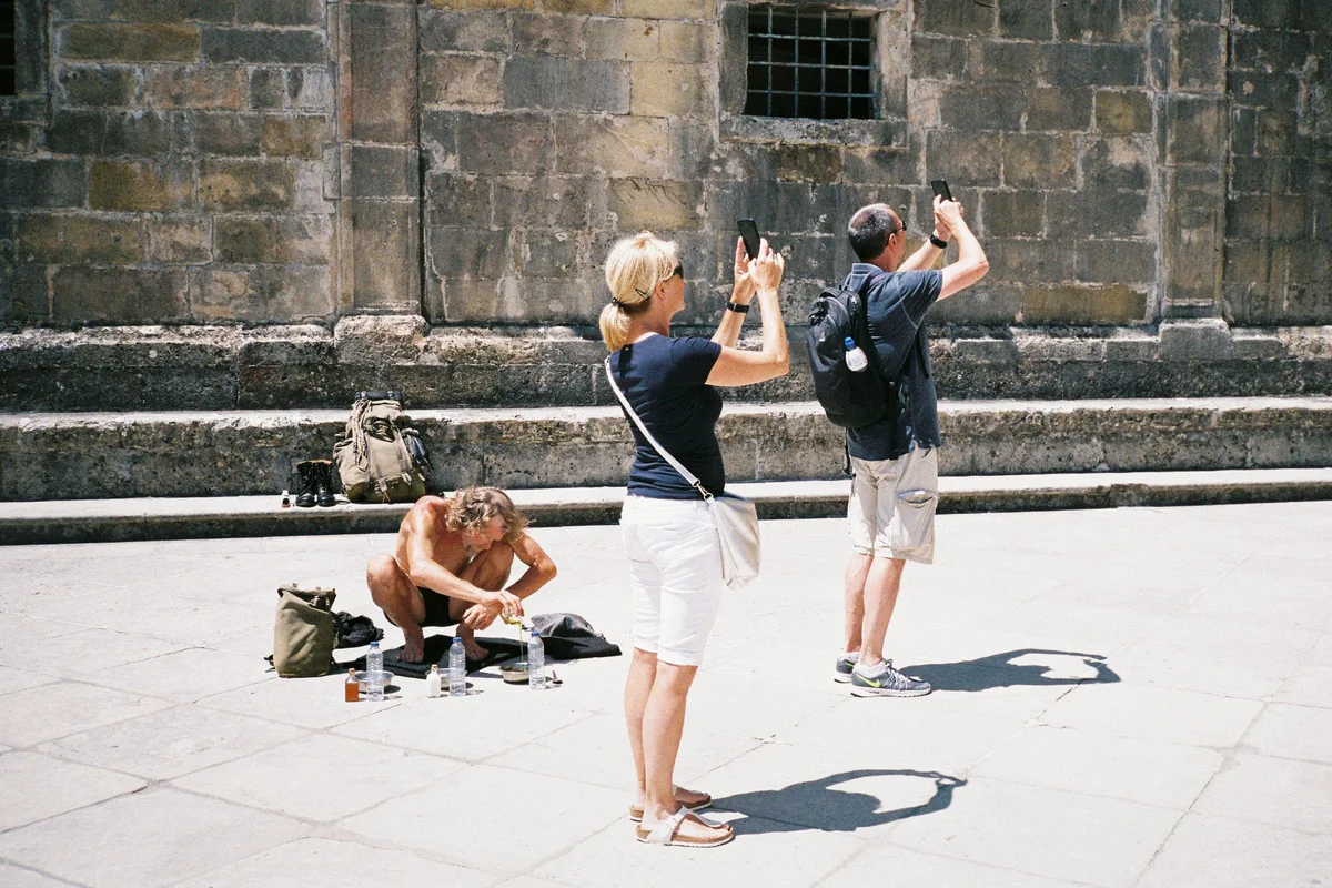 GABRIEL: zwei Touristen fotografieren einen am Boden sitzenden Performer vor einer Kirchenfassade