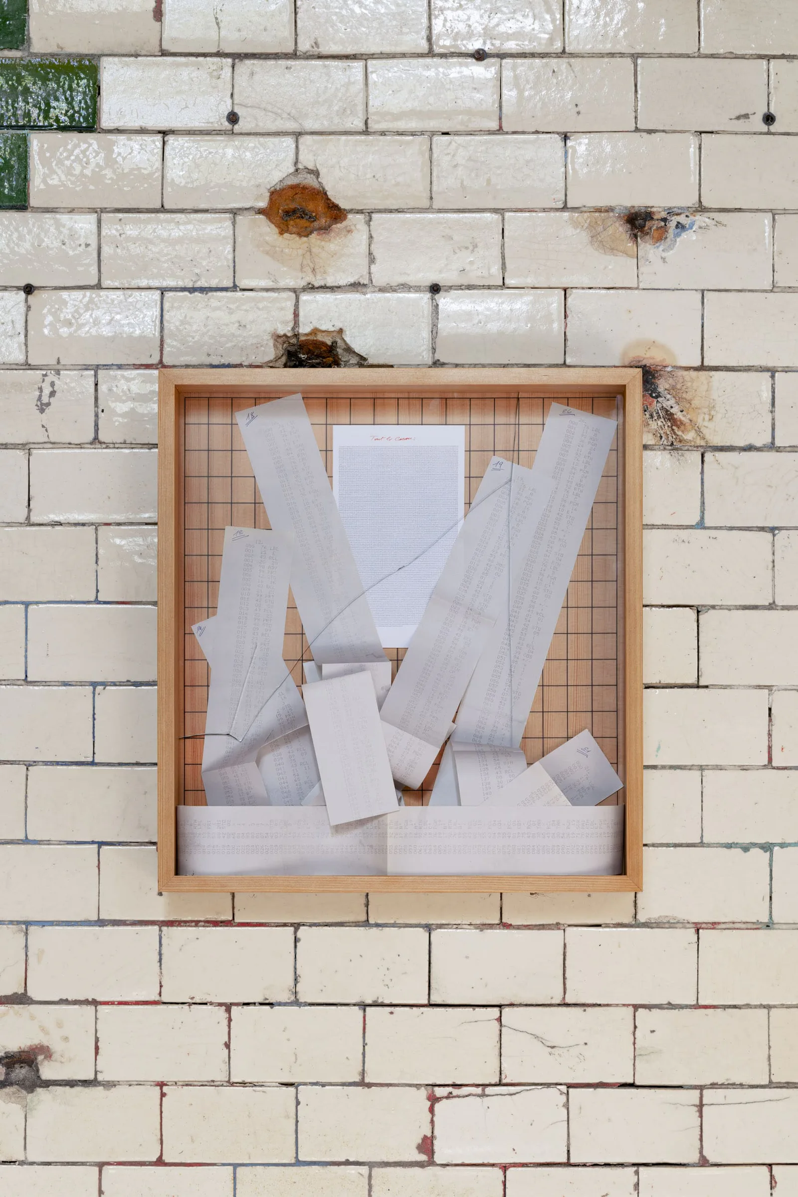 Neue Erinnerungen: gerahmtes Bild mit zerknitterten Papierstreifen an einer Kachelwand