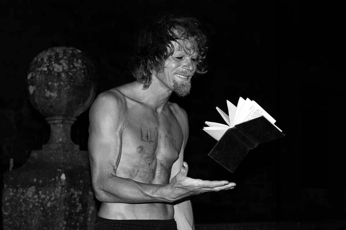 GABRIEL: Mann mit nacktem Oberkörper hält bei Nacht ein aufgeschlagenes Buch, Schwarz-Weiß