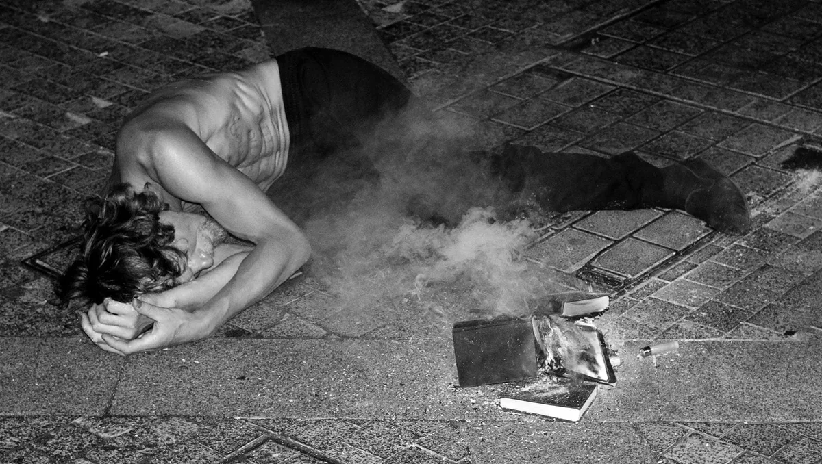 GABRIEL: Mann beugt sich bei Nacht über Bücher auf dem Boden, Rauch steigt auf, Schwarz-Weiß