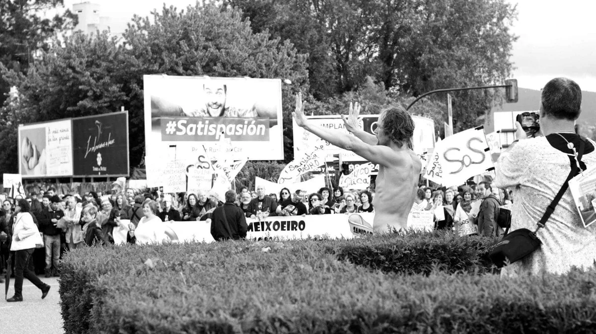GABRIEL: Performer mit nacktem Oberkörper zwischen Demonstranten mit Transparenten, Schwarz-Weiß