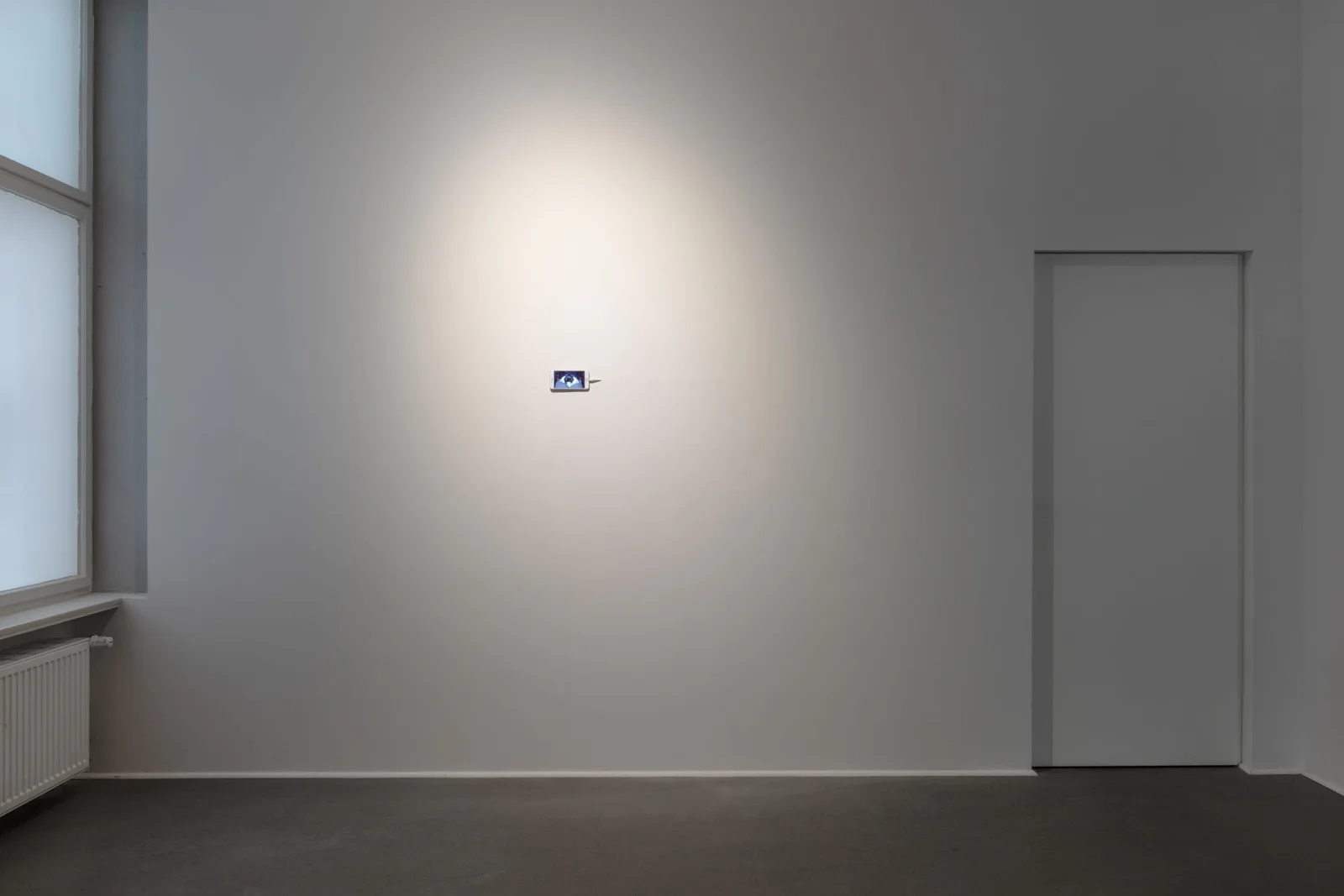 Installationsansicht: ein kleines Smartphone allein an einer großen weißen Wand