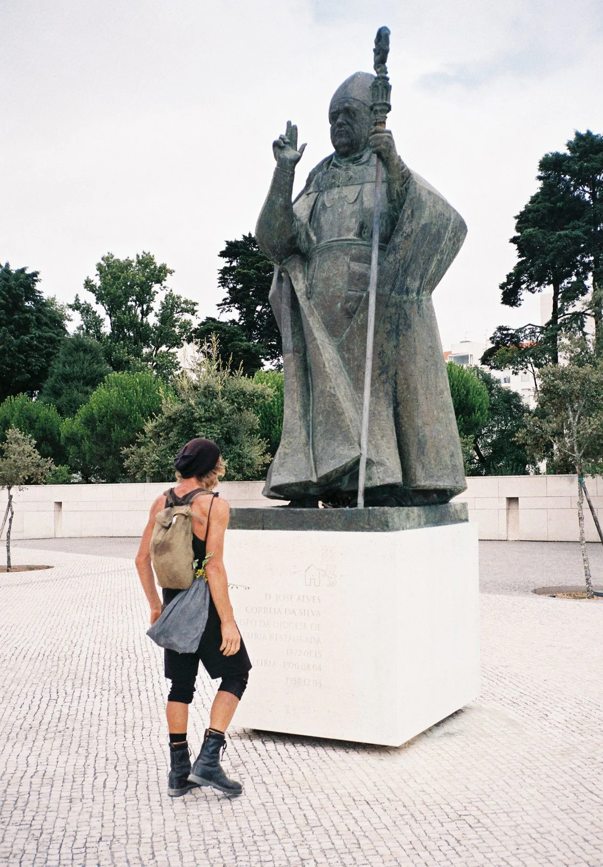 GABRIEL: Wanderer mit Rucksack neben der Statue eines segnenden Bischofs