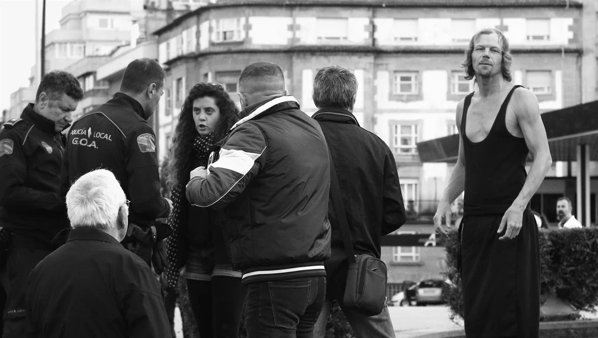 GABRIEL: Polizisten, eine Frau und ein Mann in Unterhemd auf einer Straße, Schwarz-Weiß