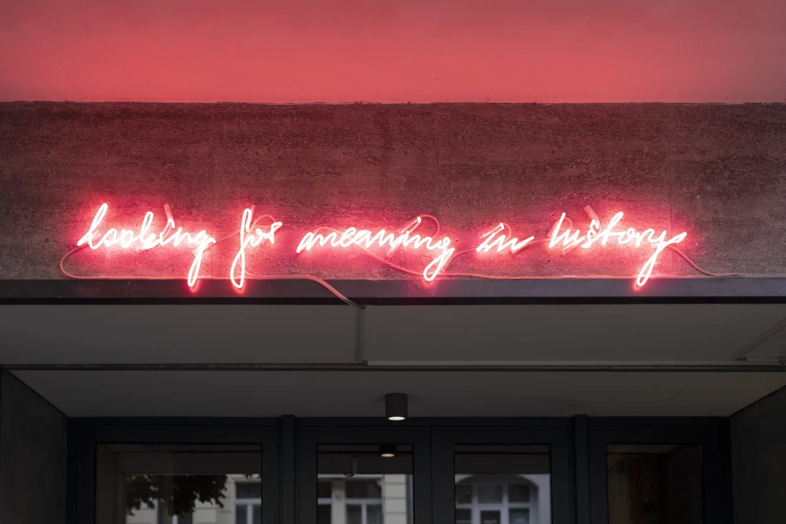 Installationsansicht: rote Neonschrift „looking for meaning in history“ über dem Eingang einer Galerie