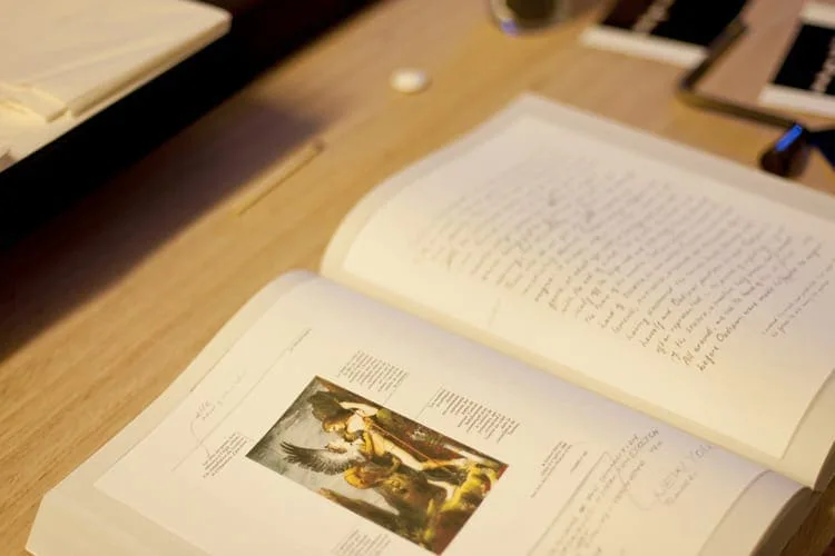 Aufgeschlagenes Buch auf einem Tisch, darin eine kleine farbige Abbildung einer Renaissance-Szene