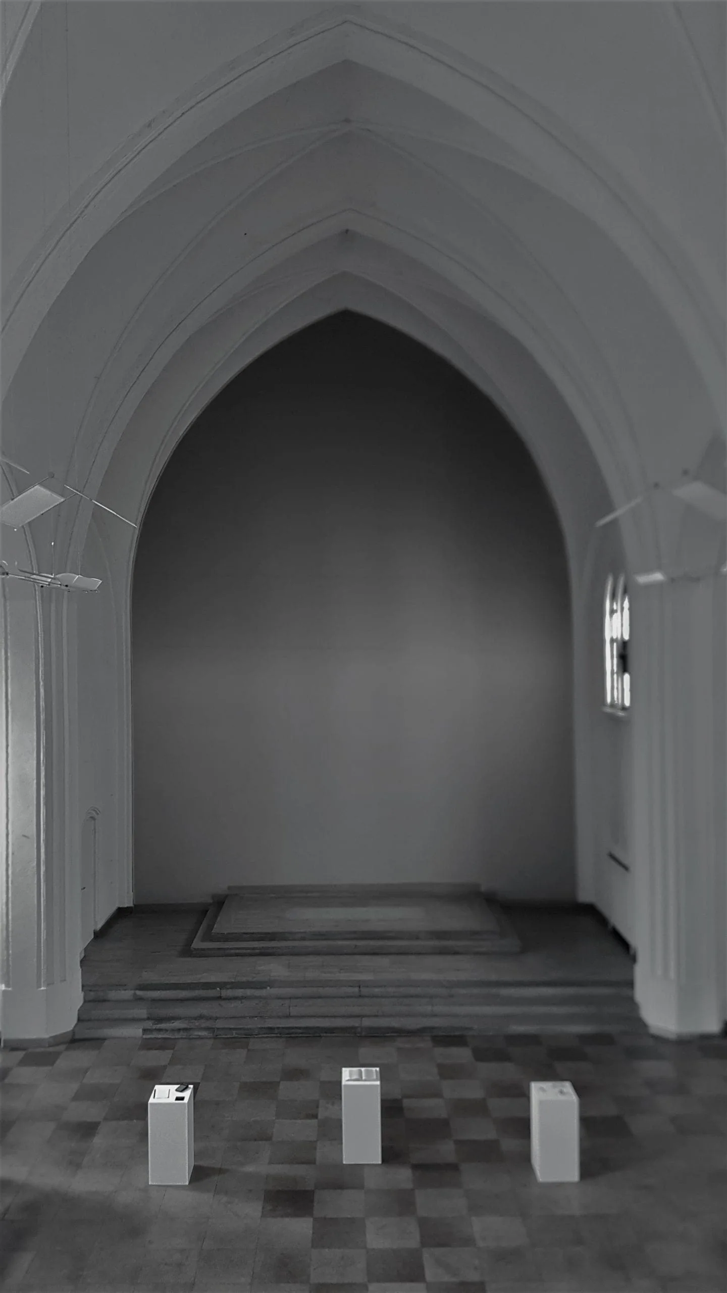 Elies Miniatures in der Friedenskirche: Blick durch einen Spitzbogen auf drei weiße Sockel auf Schachbrettboden