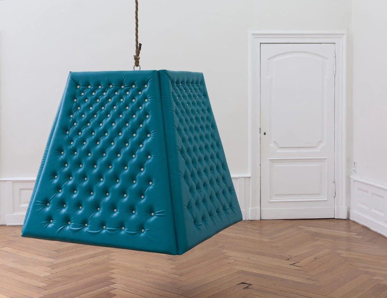 Gabo Camnitzer – The Motivator, 2011: türkisfarbenes gepolstertes Pyramidenobjekt mit Knöpfen, an einem Seil hängend