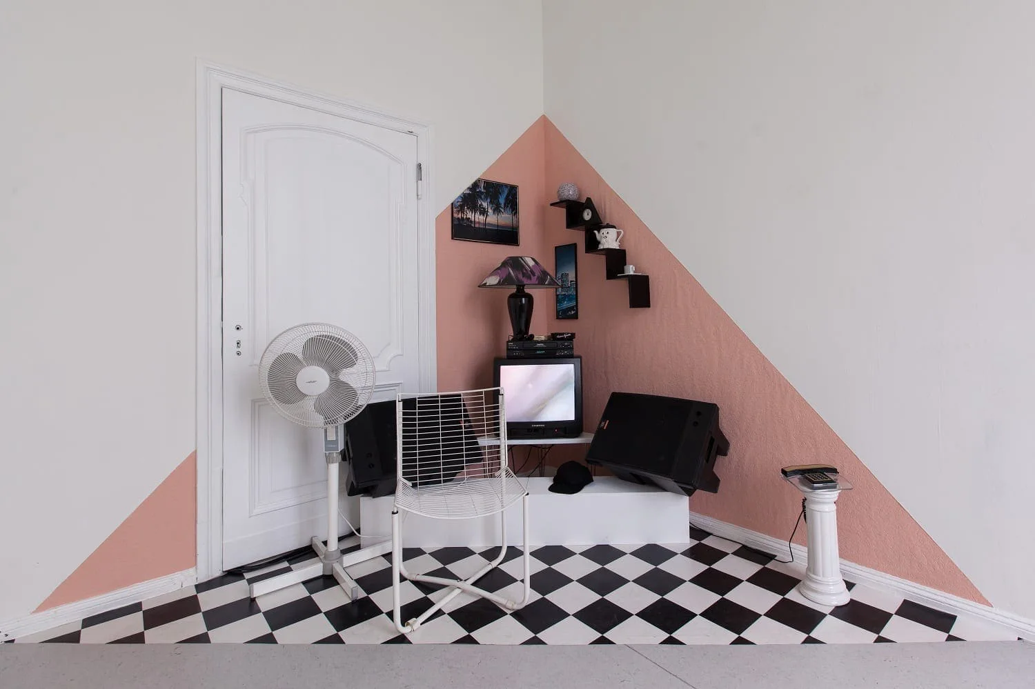 Henrike Naumann, Triangular Stories (Ibiza), 2012: Zimmerecke mit rosa Dreieck an der Wand, Ventilator, Fernseher und Schachbrettboden