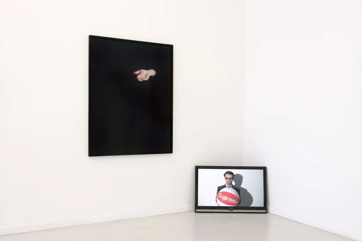 What remains the poets provide, Installationsansicht: schwarzes Bild mit einer offenen Hand an der Wand, am Boden ein gerahmtes Bild