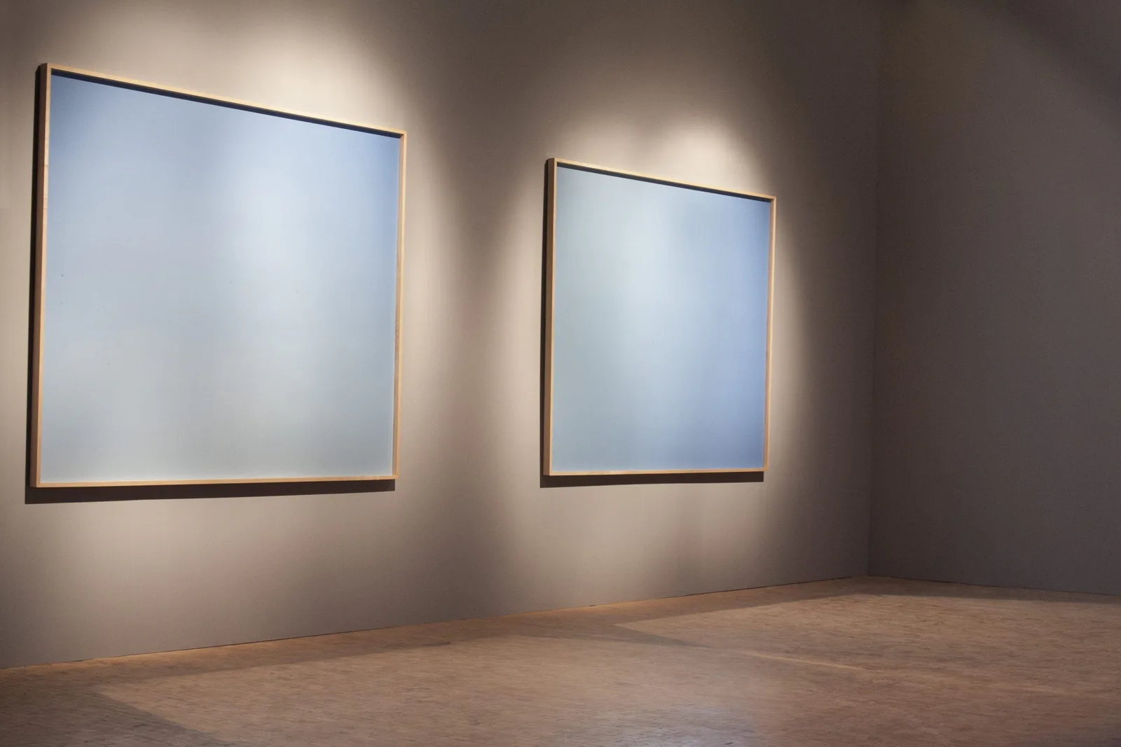 Installationsansicht: zwei große hellblaue Bilder an einer Wand unter Spotlicht