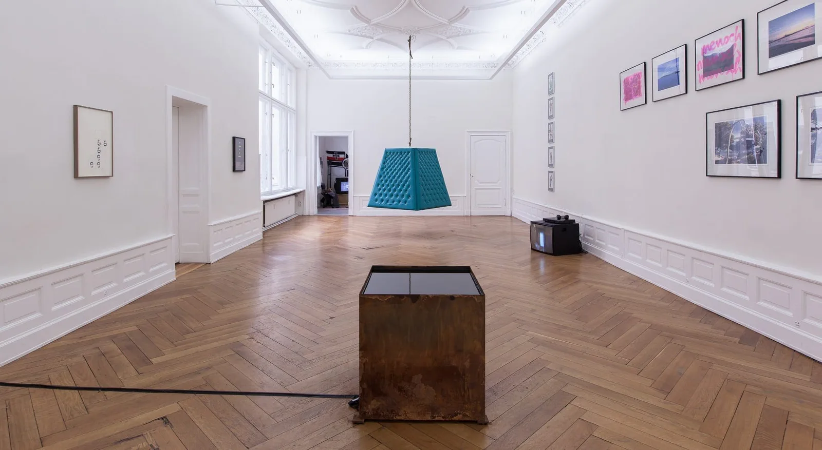 Installationsansicht in den Kunstsaelen Berlin: Altbauraum mit Parkett, türkisfarbenem Pyramidenobjekt, einem Holzkasten und Bildern an den Wänden