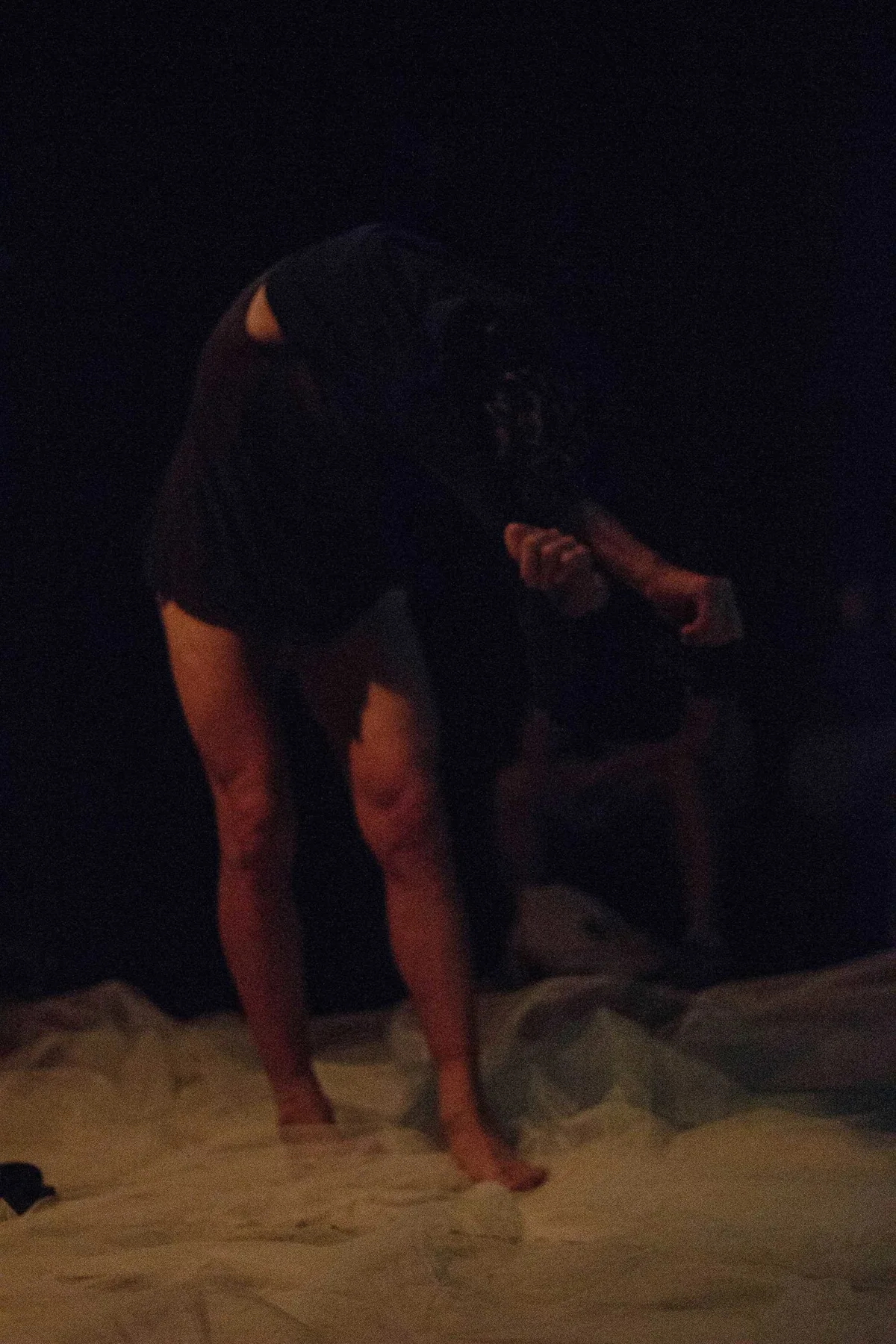 GABRIEL, Bühnenperformance: Performer in schwarzem Hemd steht gebeugt auf weißem Tuch im Dunkeln