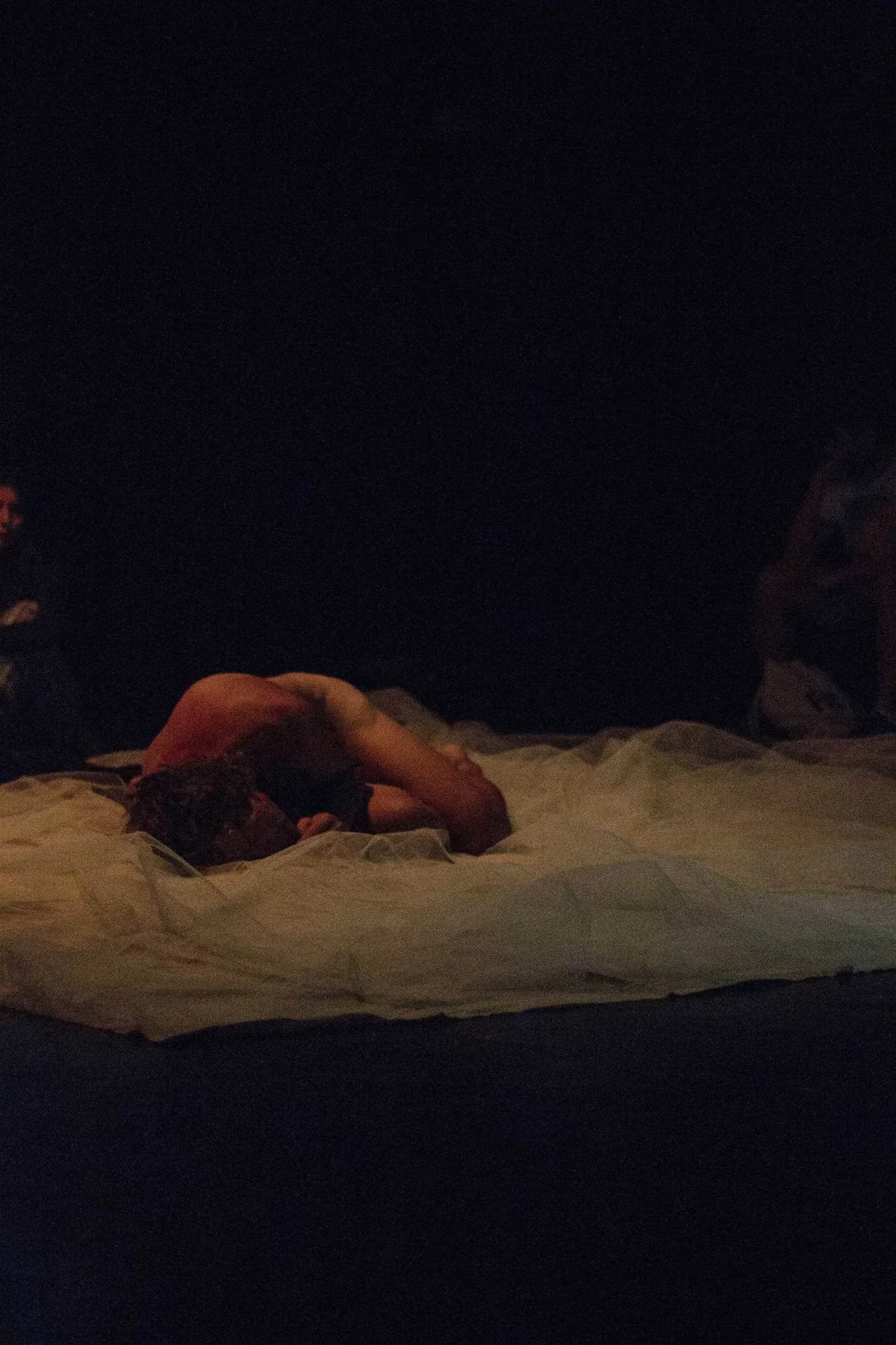 GABRIEL, Bühnenperformance: nackter Performer liegt zusammengerollt auf weißem Tuch