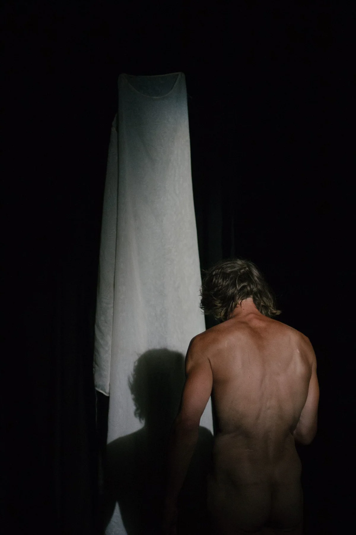 GABRIEL, Bühnenperformance: nackter Performer von hinten vor einem beleuchteten weißen Vorhang