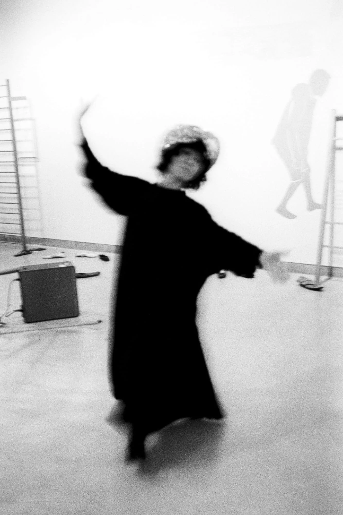 MNEMOSYNE Prelude – Die Könige: Performerin in schwarzem Gewand tanzt mit ausgebreiteten Armen in einem hellen Saal, Schwarz-Weiß
