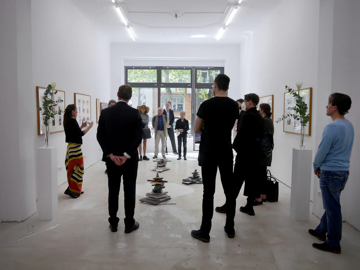GABRIEL, Ausstellungseröffnung: Besucher in einem hellen Galerieraum mit gerahmten Fotografien und Pflanzen auf Sockeln