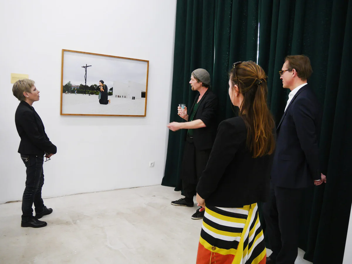 GABRIEL, Ausstellung: Besucher im Gespräch vor einer großen Fotografie, daneben ein dunkelgrüner Vorhang