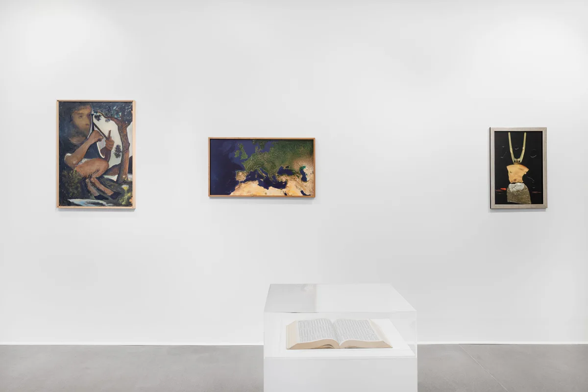 Ausstellungsansicht: drei Gemälde von Hilarion Manero an einer weißen Wand, davor ein aufgeschlagenes Buch auf einem Sockel
