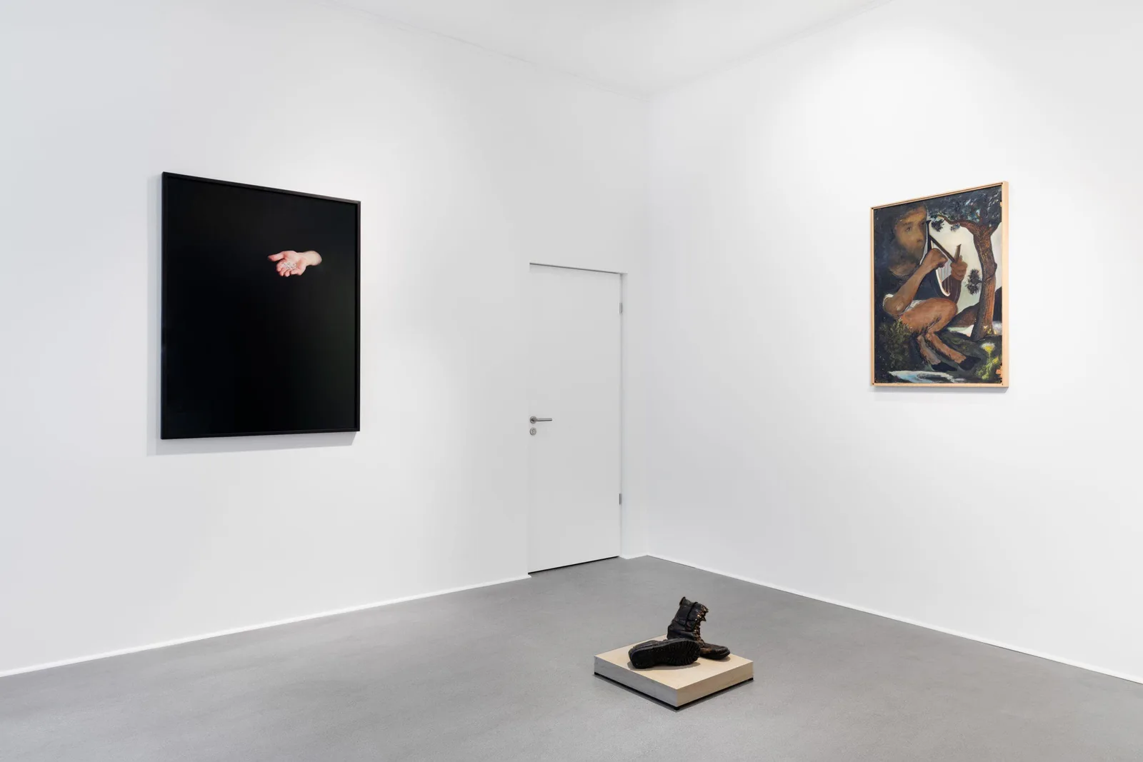 Ausstellungsansicht: weißer Raum mit zwei Gemälden, einer Tür und einem Objekt am Boden