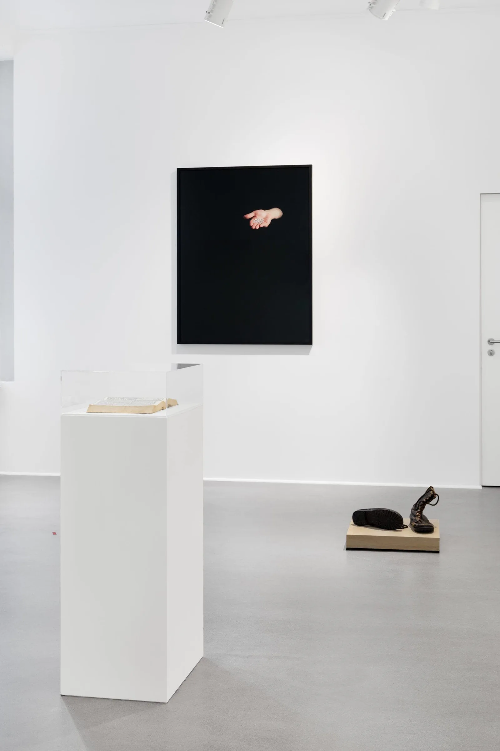 What remains the poets provide, Installationsansicht: schwarzes Bild mit offener Hand, ein Sockel und ein Objekt am Boden