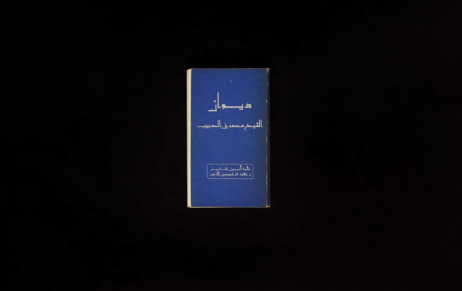 Der Diwan des Shaykh Muhammad Ibn Al Habib (1876–1981): ein kleines blaues Buch mit arabischem Titel vor schwarzem Hintergrund