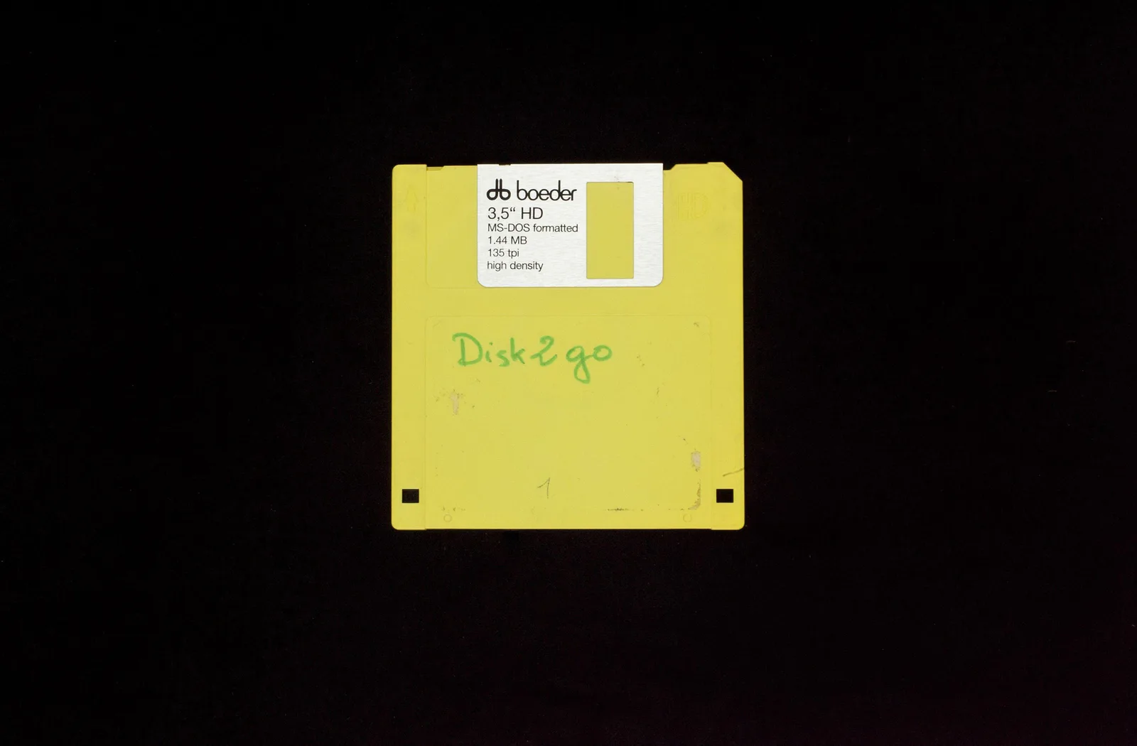 DISK2GO: eine gelbe 3,5-Zoll-Diskette mit handschriftlicher Beschriftung vor schwarzem Hintergrund
