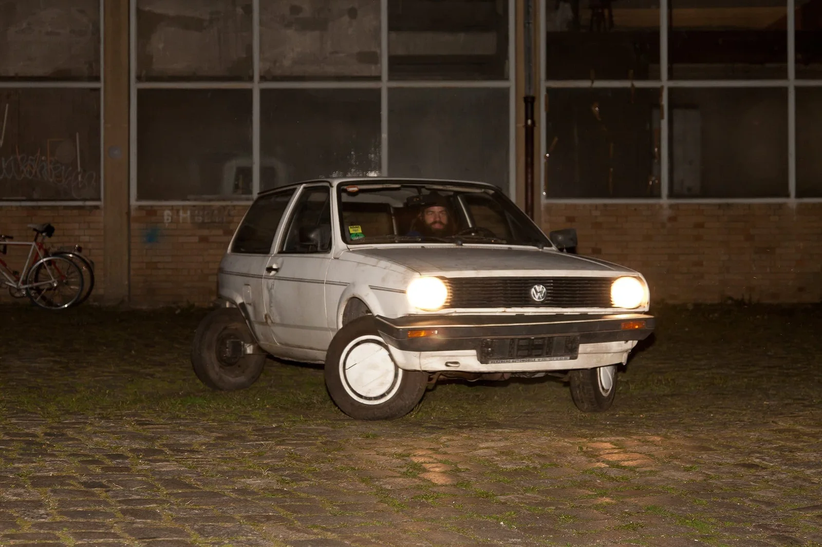 Handlungsbereitschaft – Skizze einer Generation am Ende der Geschichte: ein Kleinwagen bei Nacht auf Kopfsteinpflaster vor einer Fabrikfassade