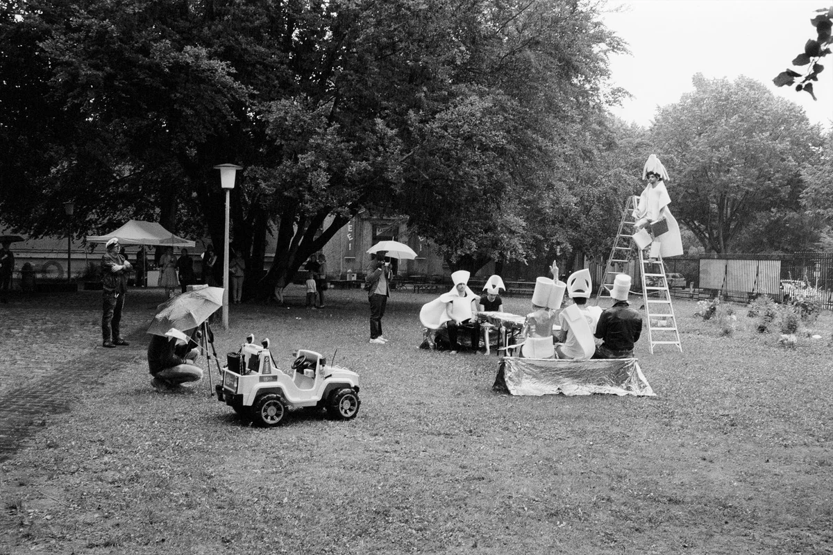 Schwarz-Weiß-Foto einer Versammlung unter Bäumen im Park mit Leiter, Spielzeugauto und Besuchern auf Decken