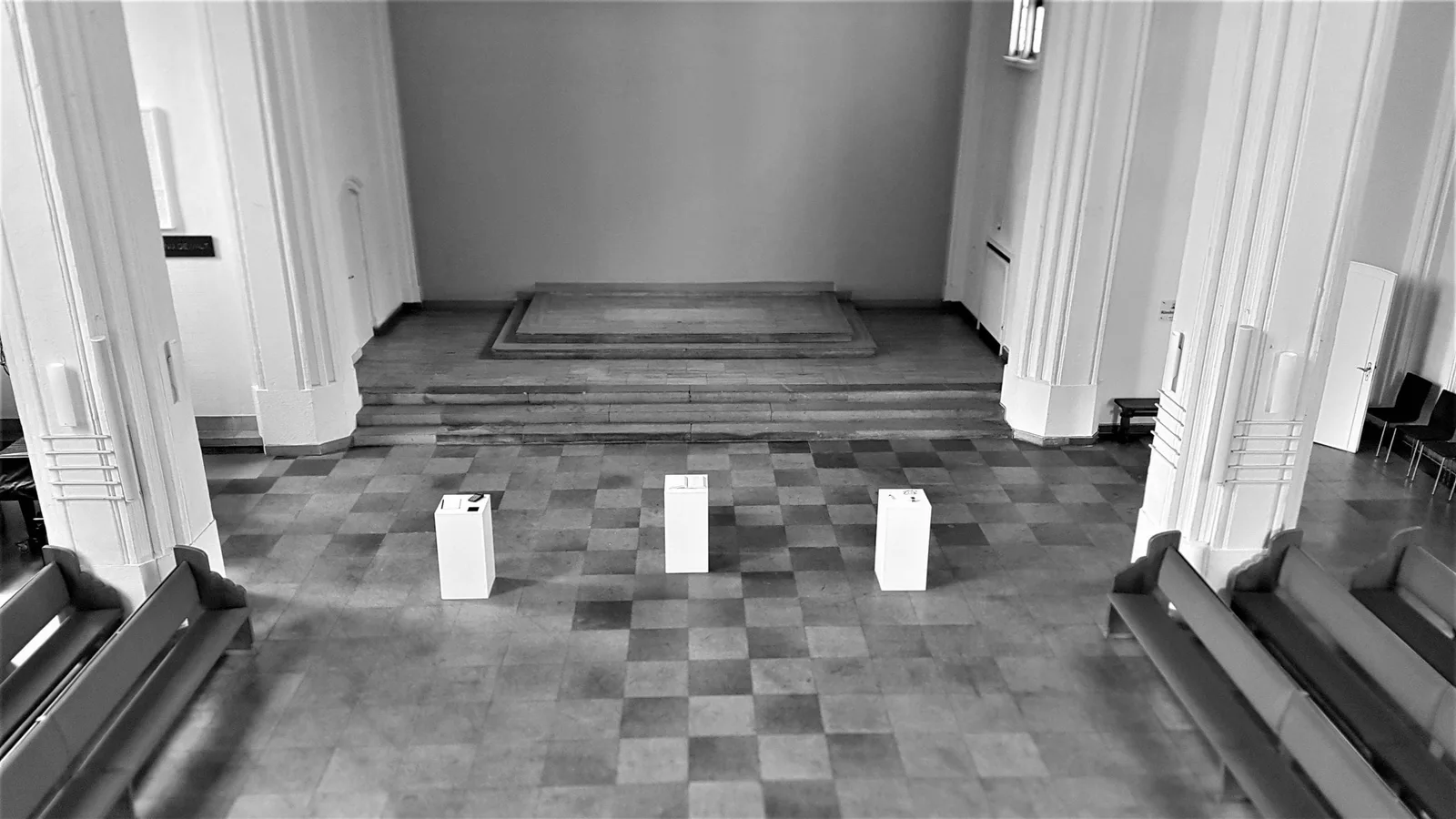 Kirchenraum der Friedenskirche mit drei weißen Sockeln auf Schachbrettboden, Schwarz-Weiß
