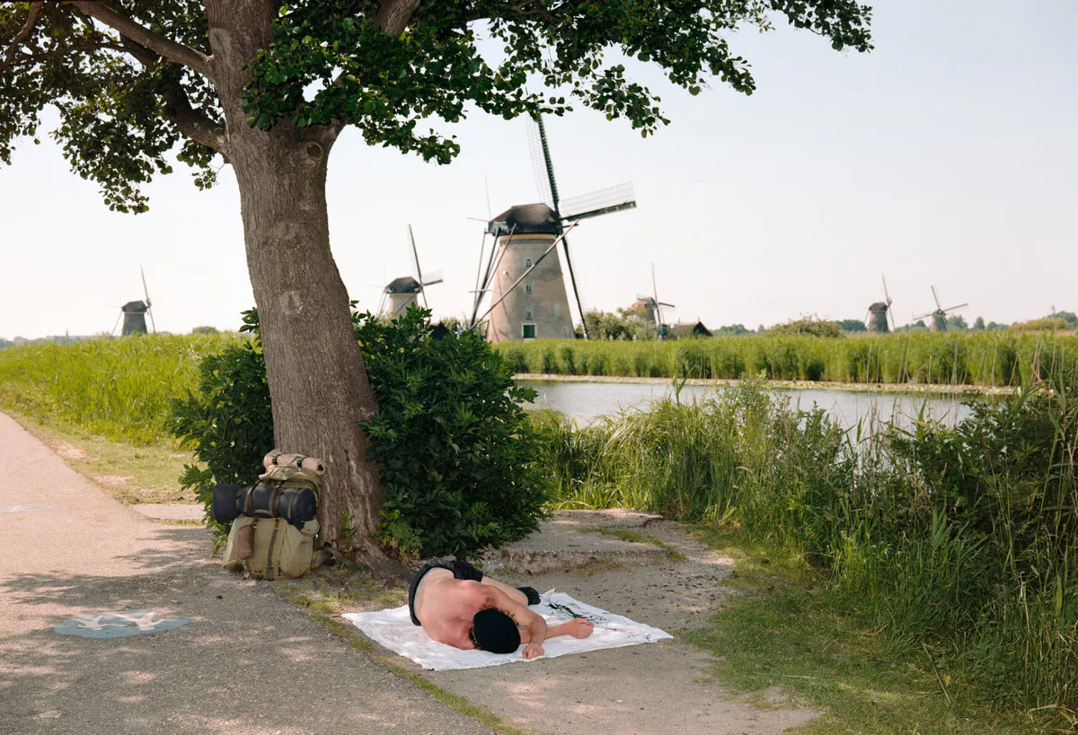 GABRIEL: Mann liegt auf einem Tuch unter einem Baum, dahinter Windmühlen von Kinderdijk
