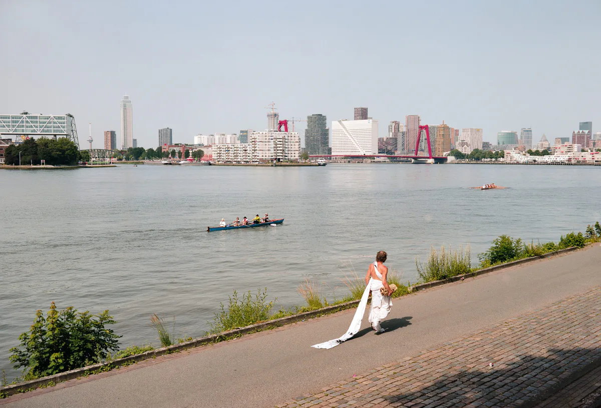 GABRIEL: Mann zieht eine lange weiße Stoffbahn am Ufer der Maas entlang, dahinter die Skyline von Rotterdam