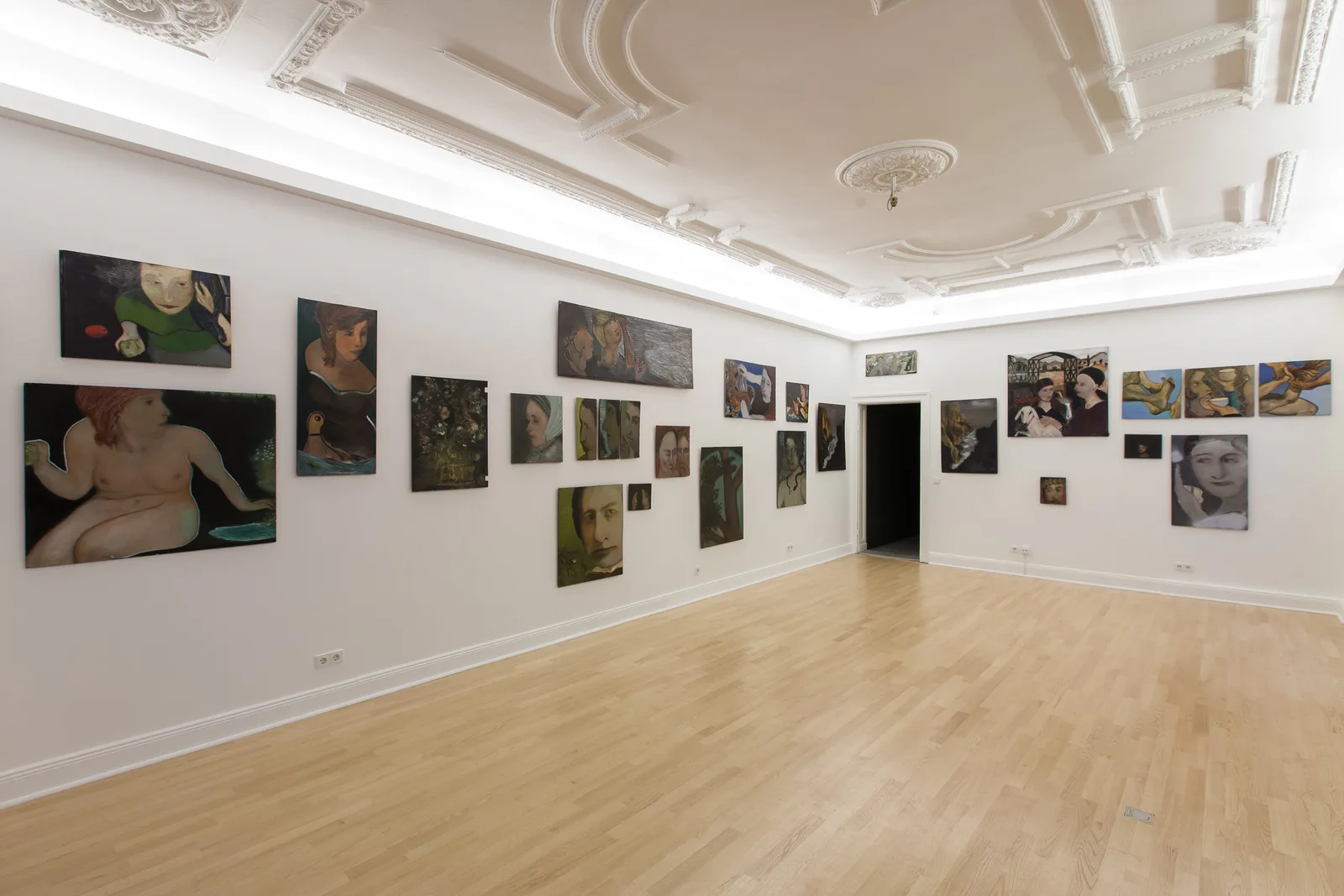 Installationsansicht: Altbausaal mit Stuckdecke, Parkett und vielen Gemälden von Hilarion Manero an den Wänden