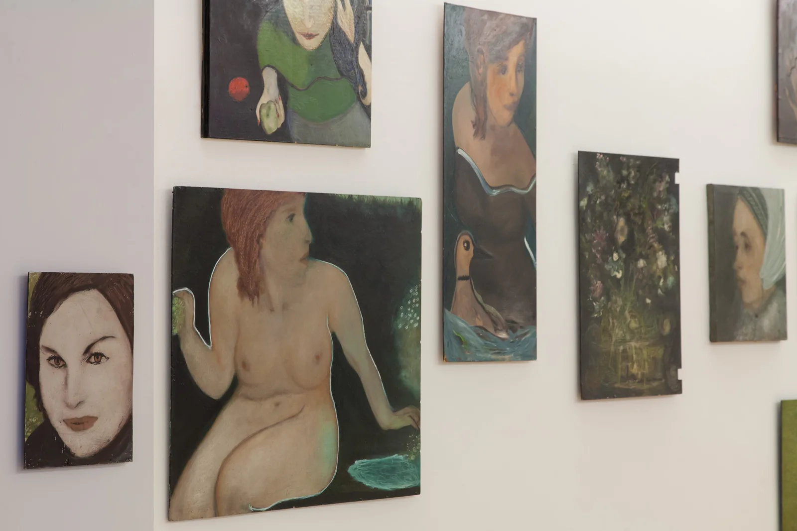 Installationsansicht: Gemälde von Hilarion Manero mit Frauengesichtern und Akten an einer weißen Wand