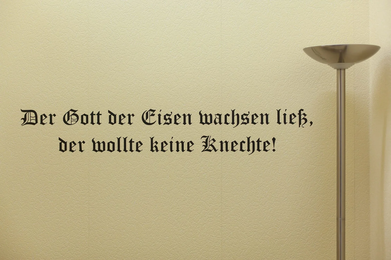 Henrike Naumann, Unbetitelt, 2013: Spruch in Frakturschrift an einer Wand „Der Gott der Eisen wachsen ließ, der wollte keine Knechte!“, daneben eine Stehlampe