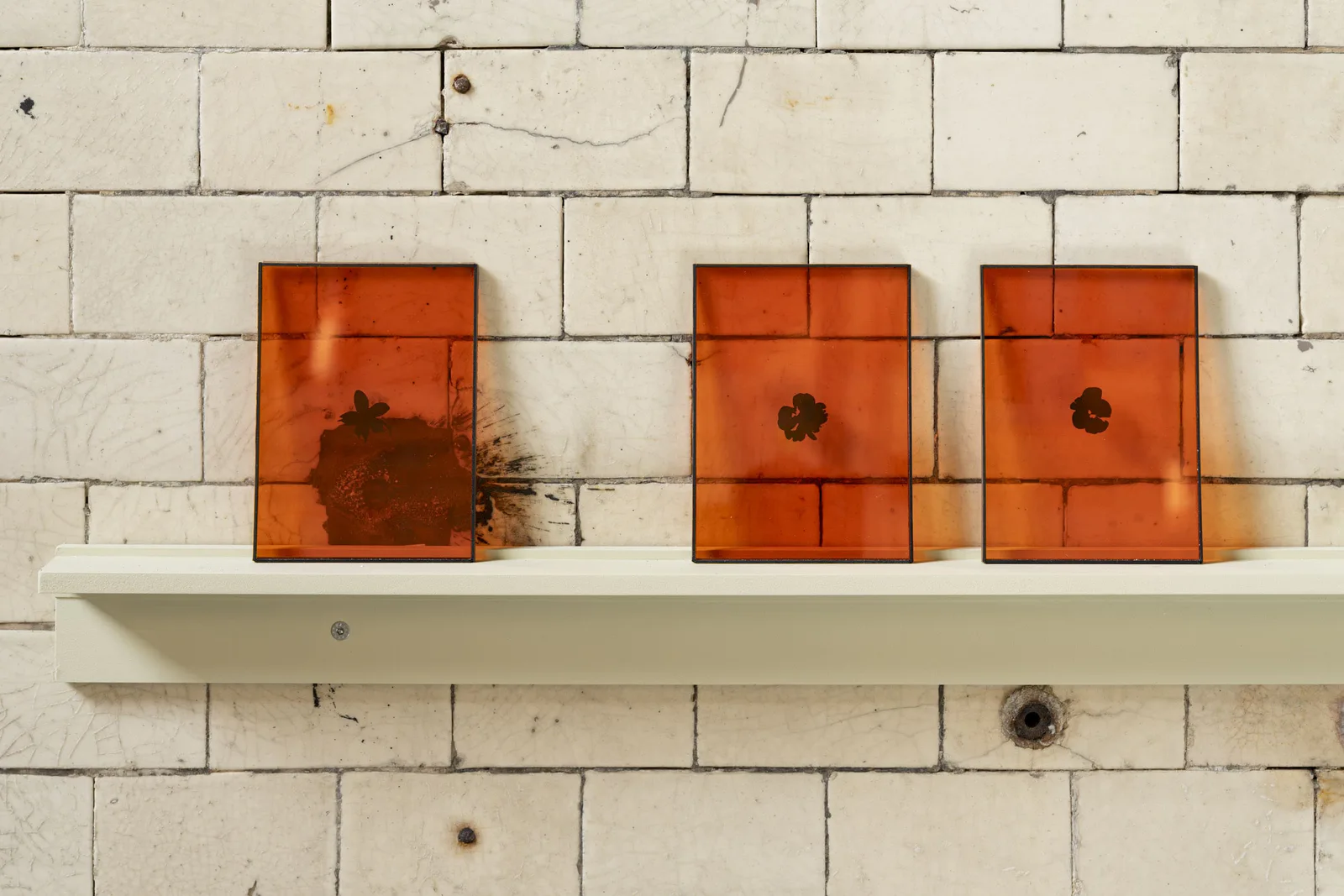 Ben Greber, „Mr. & Mrs. Bouqdib“, 2024: drei orangefarbene Glasplatten auf einem Regalbrett vor einer gefliesten Wand