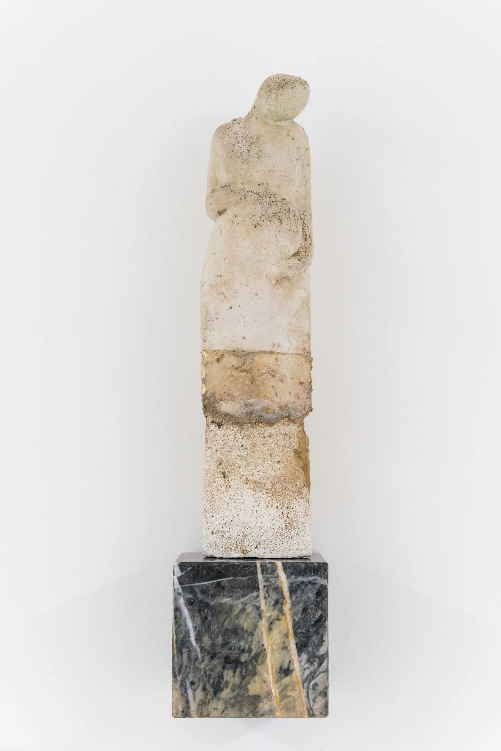 Magna Mater (Antlitz 6): verwitterte Steinfigur ohne Gesicht auf einem Sockel aus dunklem Marmor