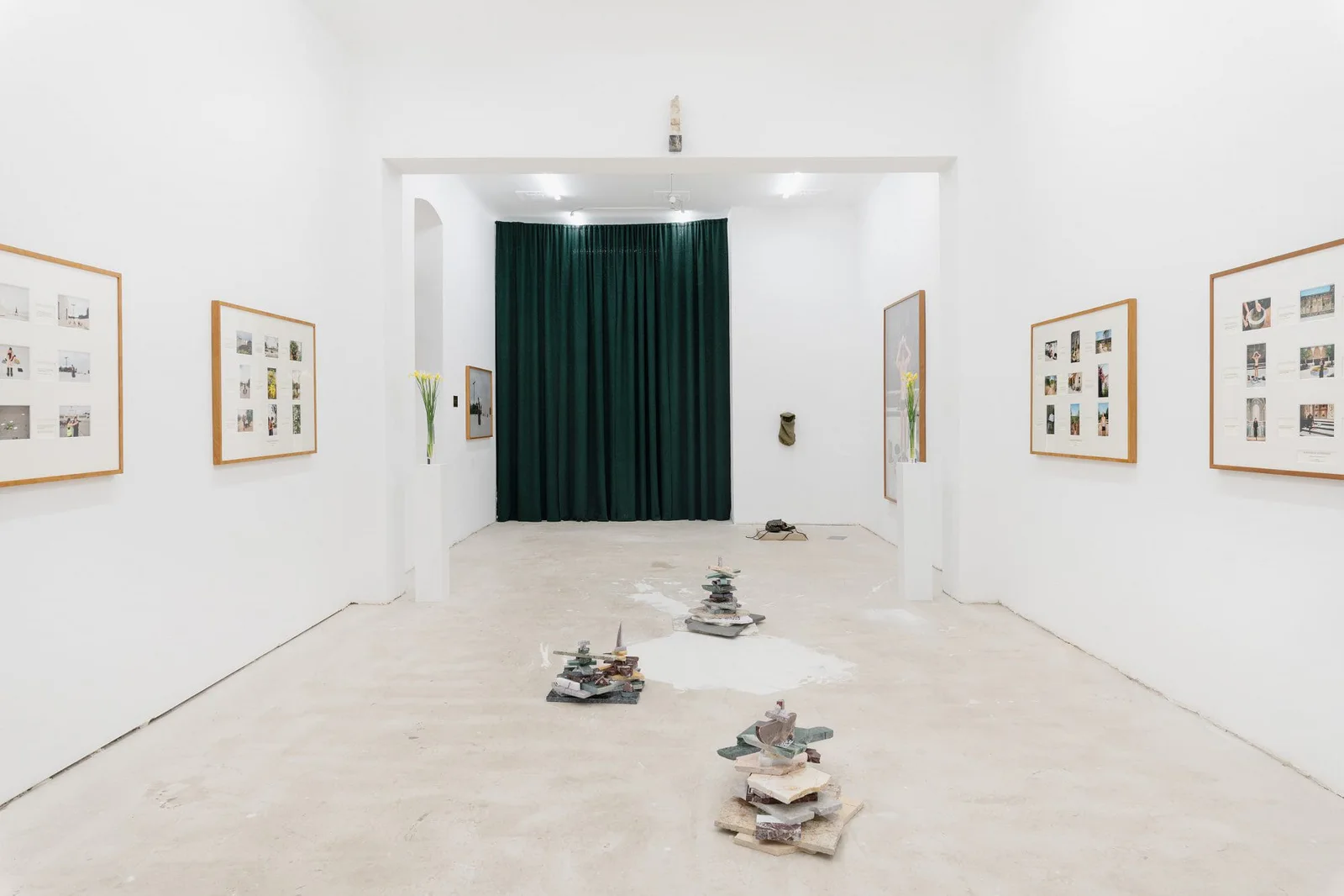 Marianische Antiphonen I – III, Ausstellungsansicht: weißer Raum mit gerahmten Tafeln, einem grünen Vorhang und Steinen am Boden