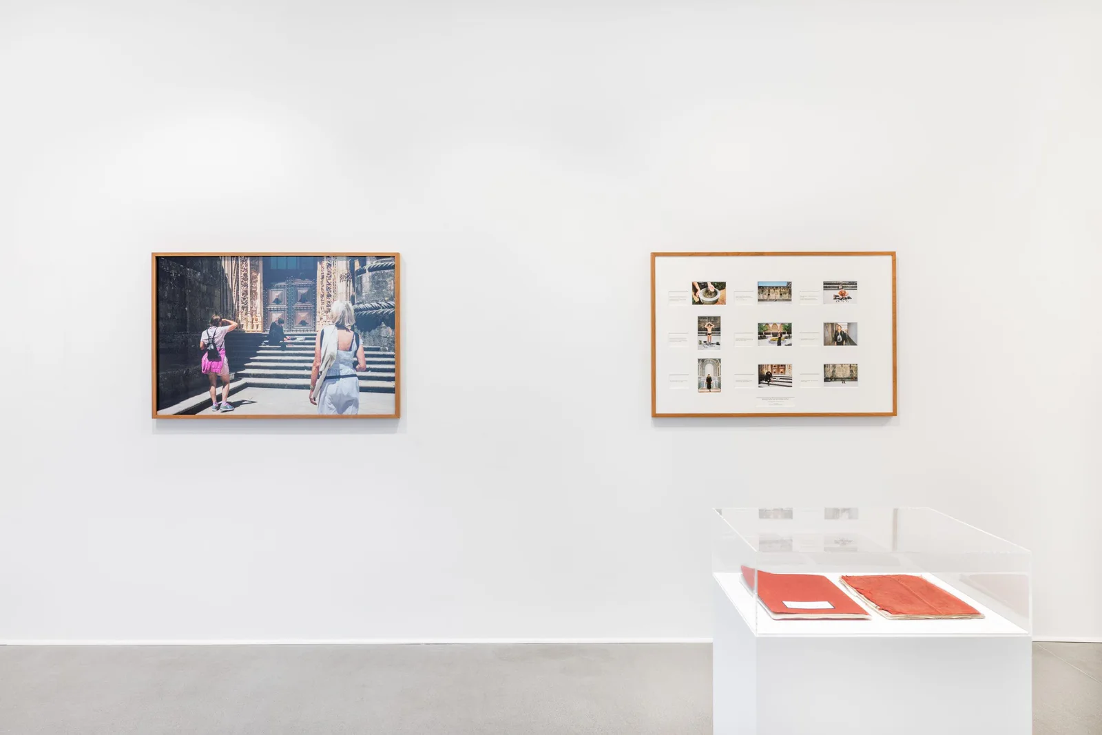 Installationsansicht: gerahmte Fotografie, eine Tafel mit kleinen Bildern und eine Vitrine mit roten Büchern in einem weißen Raum