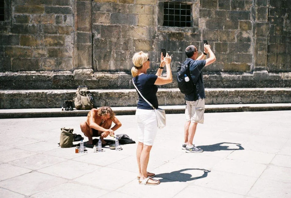 GABRIEL: ein Mann kniet vor einer Kirchenmauer, zwei Touristen fotografieren ihn