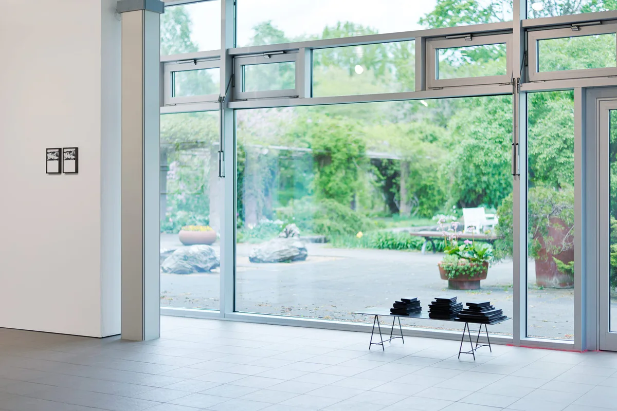 The road leads back and back to the black square: Ausstellungsraum mit Glasfront zum Garten, kleine Rahmen an der Wand und eine Bank