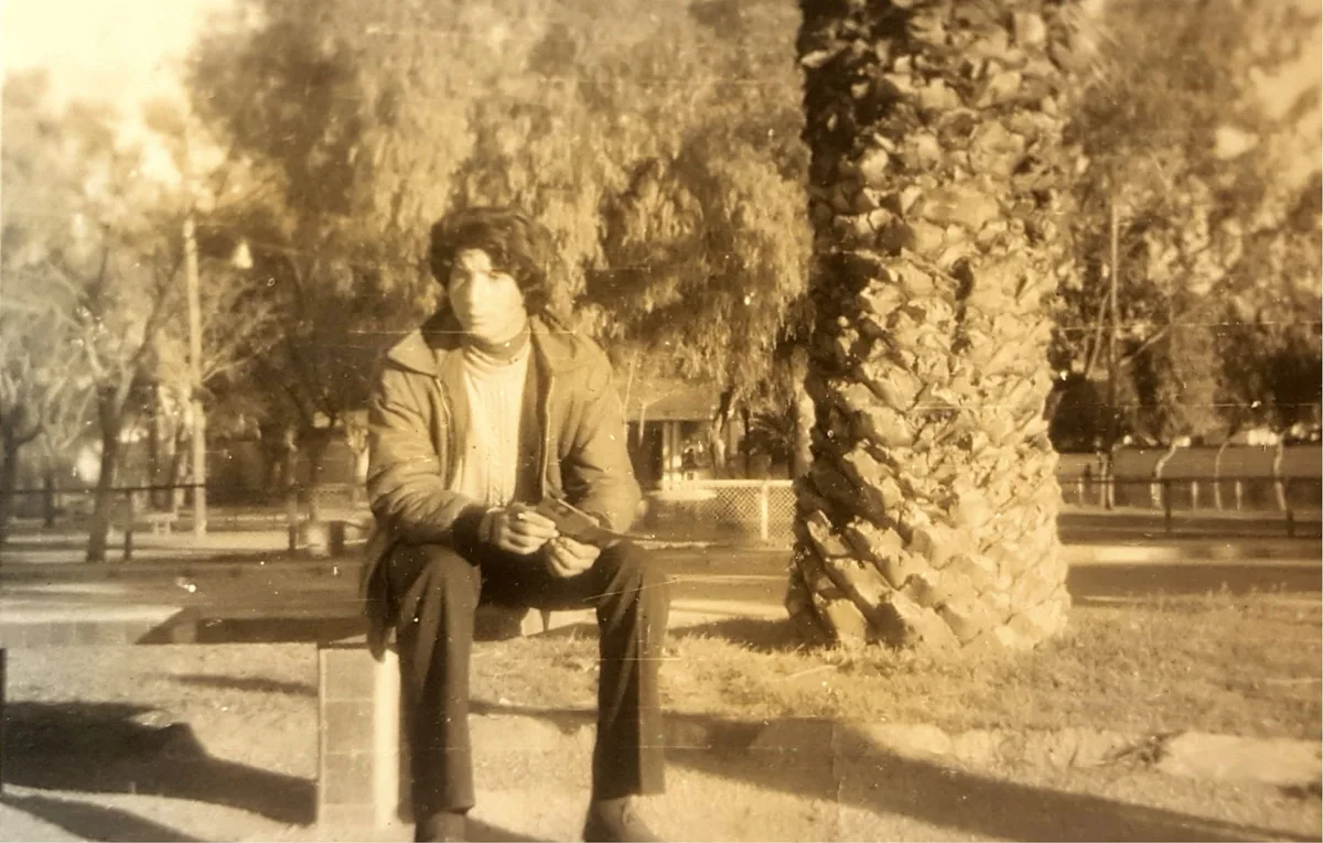 El Arbi Bouqdib as a young man on a bench beneath palm trees, old sepia photograph