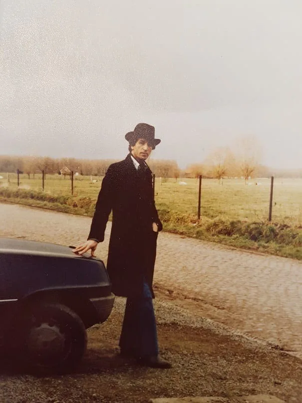 El Arbi Bouqdib in a hat and coat beside a car on a country road, old colour photograph