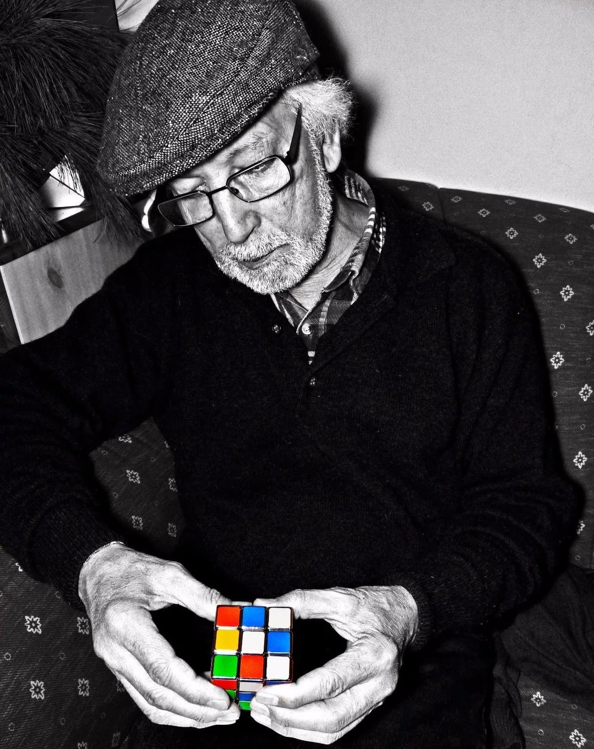 The older El Arbi Bouqdib in glasses and a cap solving a Rubik’s cube, black and white