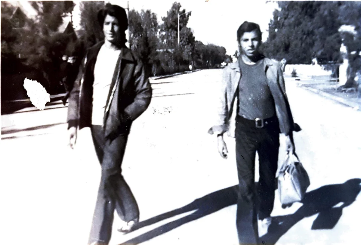 Two young men walking along a sunny street, one carrying a bag, old black-and-white photograph