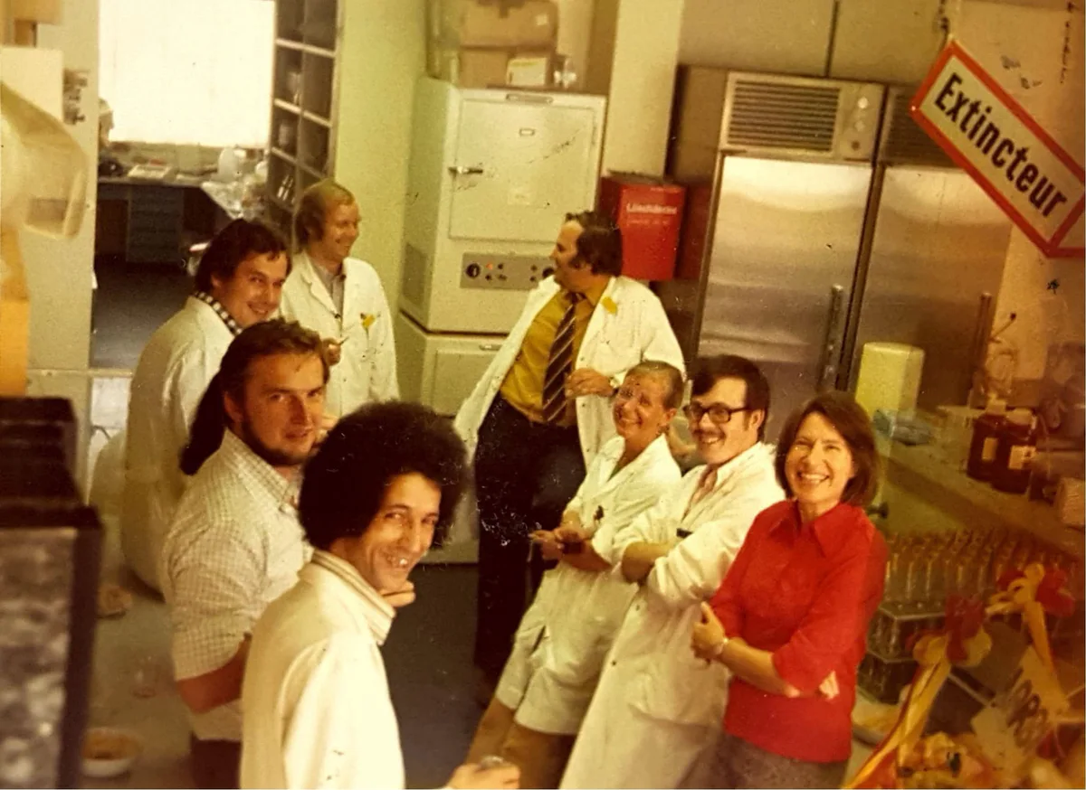 A group in white coats in a commercial kitchen with El Arbi Bouqdib in the middle, old colour photograph