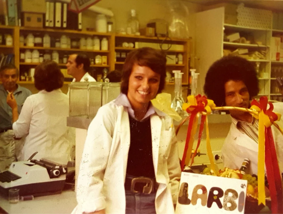 El Arbi Bouqdib with a colleague in white coats in a laboratory, a gift with ribbons and a sign reading “Larbi”, old colour photograph